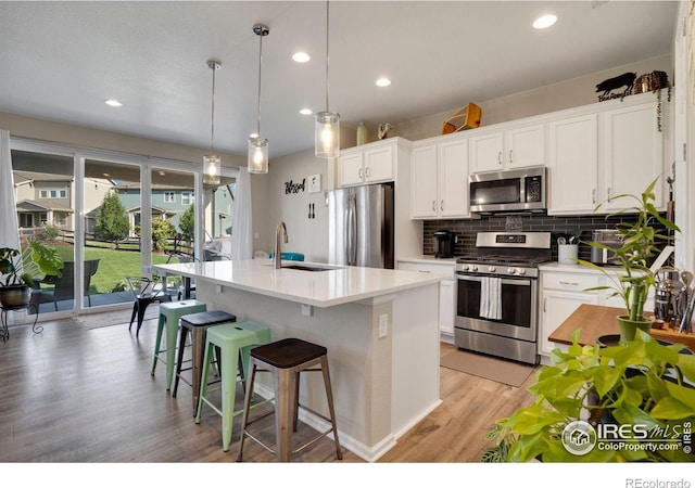 kitchen featuring white cabinets, hanging light fixtures, stainless steel appliances, sink, and a kitchen island with sink