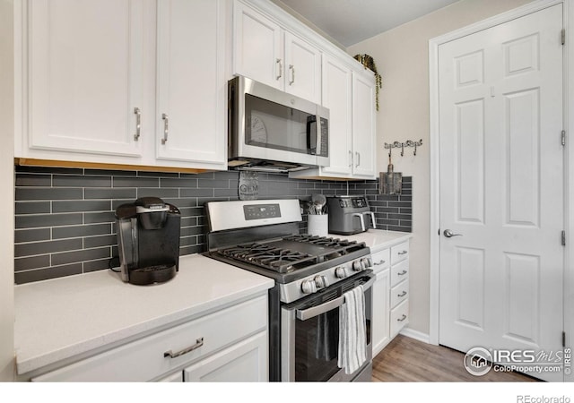 kitchen with light hardwood / wood-style flooring, appliances with stainless steel finishes, white cabinets, and tasteful backsplash