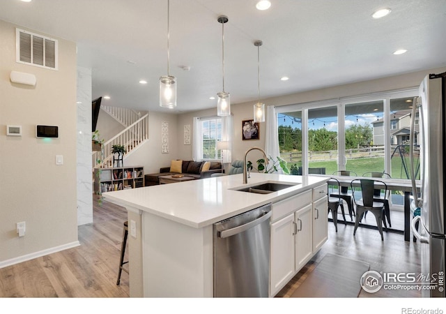 kitchen featuring white cabinetry, stainless steel appliances, sink, hanging light fixtures, and a center island with sink