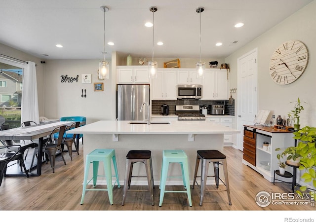 kitchen with appliances with stainless steel finishes, white cabinetry, decorative light fixtures, and a kitchen breakfast bar