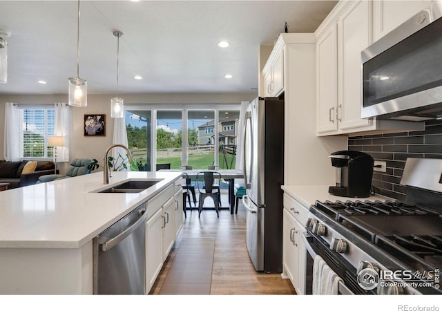 kitchen with white cabinets, appliances with stainless steel finishes, light hardwood / wood-style floors, sink, and a kitchen island with sink