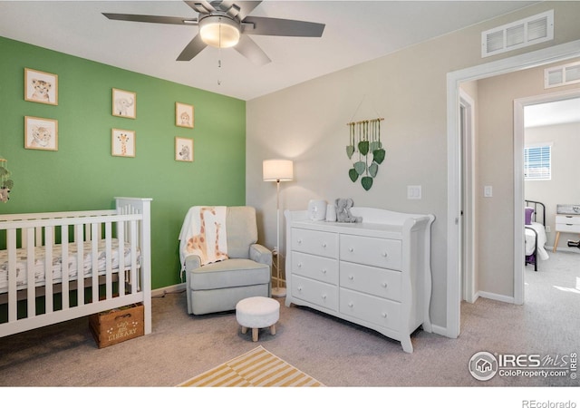 bedroom featuring light colored carpet, a nursery area, and ceiling fan