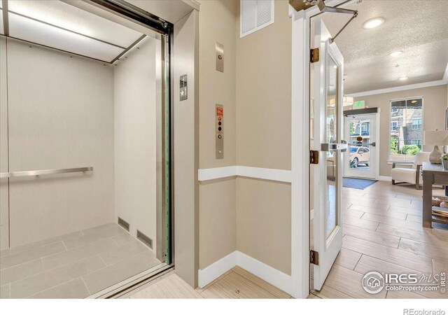 interior space with light hardwood / wood-style flooring, crown molding, a textured ceiling, and elevator