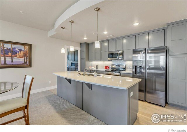 kitchen featuring decorative light fixtures, appliances with stainless steel finishes, a kitchen island with sink, sink, and decorative backsplash