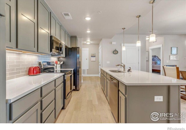 kitchen featuring a center island with sink, light hardwood / wood-style flooring, stainless steel appliances, sink, and gray cabinets