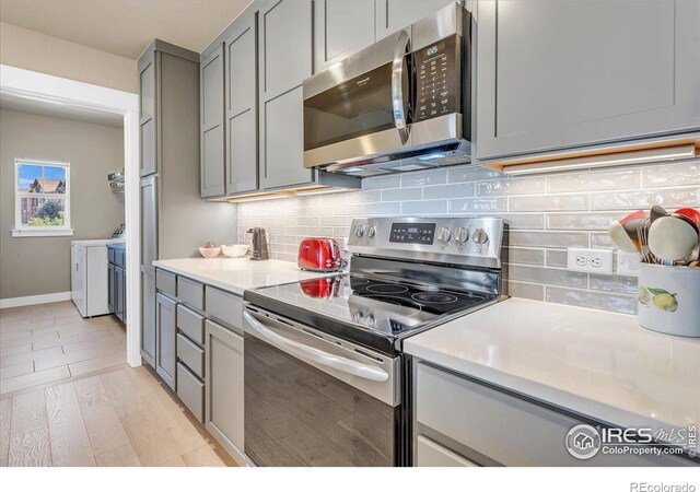 kitchen with light hardwood / wood-style flooring, backsplash, washer and dryer, stainless steel appliances, and gray cabinets