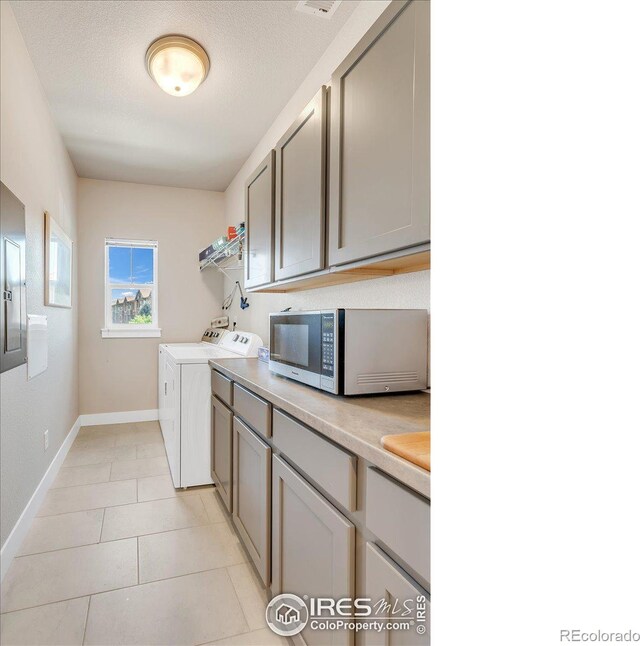 clothes washing area with a textured ceiling, washer and clothes dryer, and light tile patterned floors