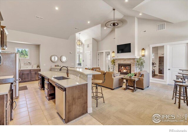 kitchen featuring a kitchen island with sink, high vaulted ceiling, a brick fireplace, sink, and appliances with stainless steel finishes