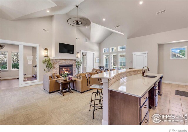 kitchen with a fireplace, sink, high vaulted ceiling, a kitchen island with sink, and a breakfast bar