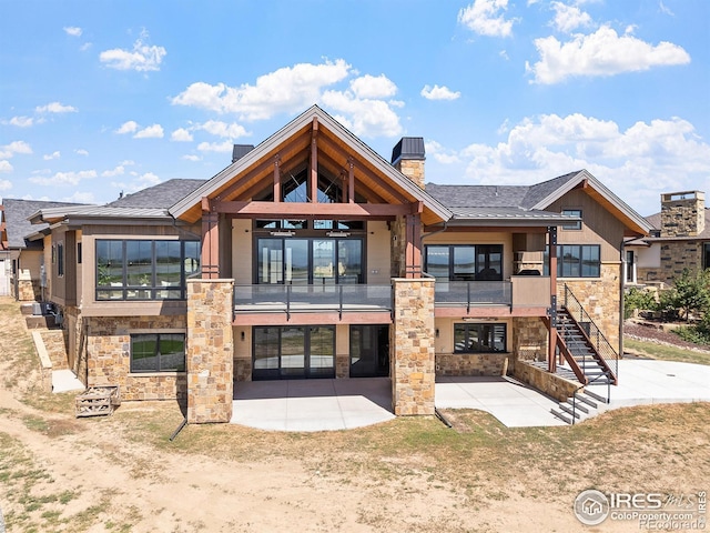 back of property with stone siding, a patio area, stairway, and a balcony