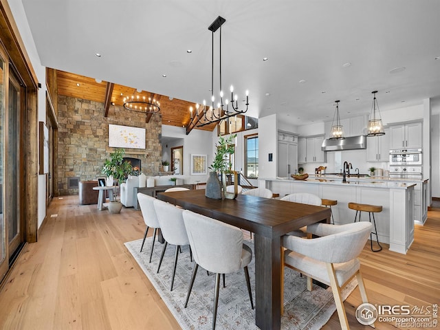 dining space with recessed lighting, light wood-style flooring, beamed ceiling, and a stone fireplace