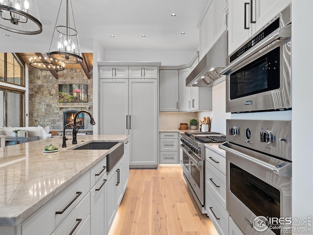 kitchen featuring range with two ovens, light wood-style flooring, hanging light fixtures, under cabinet range hood, and a fireplace