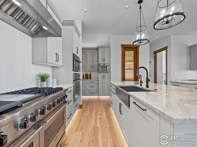 kitchen featuring light stone counters, light wood finished floors, appliances with stainless steel finishes, a sink, and wall chimney range hood