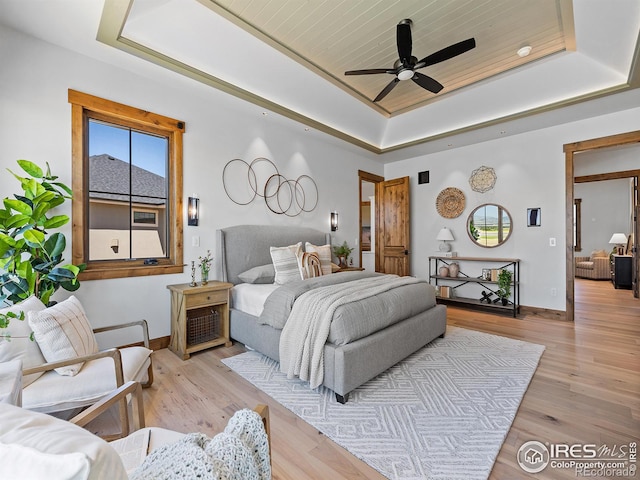 bedroom featuring a tray ceiling, baseboards, and light wood finished floors