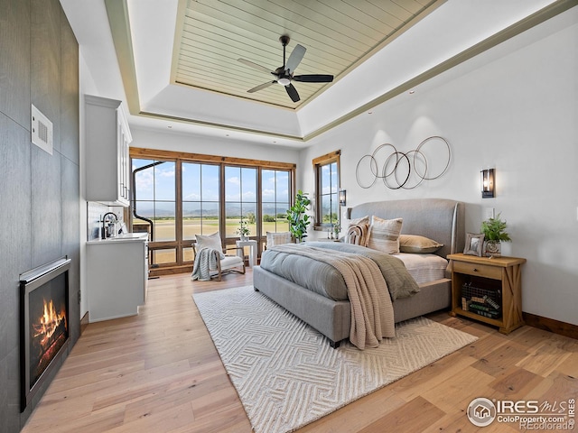 bedroom with a warm lit fireplace, visible vents, a raised ceiling, access to exterior, and light wood-type flooring