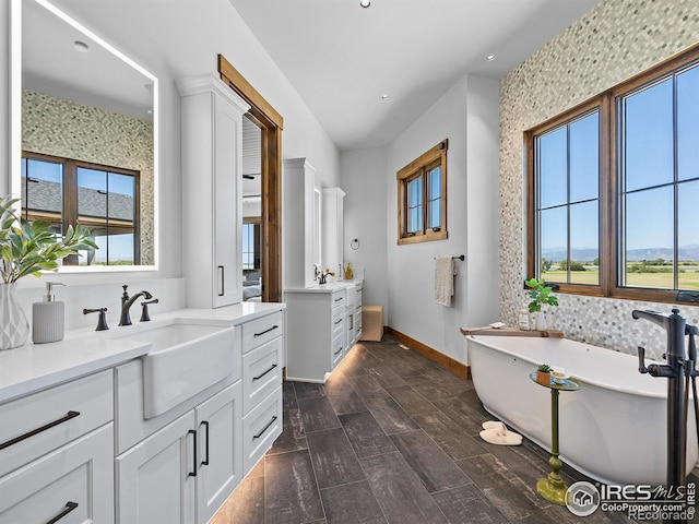 bathroom with recessed lighting, two vanities, a sink, a freestanding tub, and baseboards