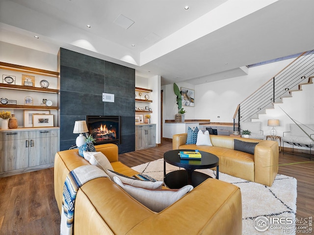 living area featuring built in features, recessed lighting, a tiled fireplace, wood finished floors, and stairs