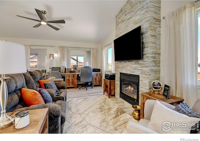 living room featuring lofted ceiling, ceiling fan, light hardwood / wood-style floors, and a stone fireplace