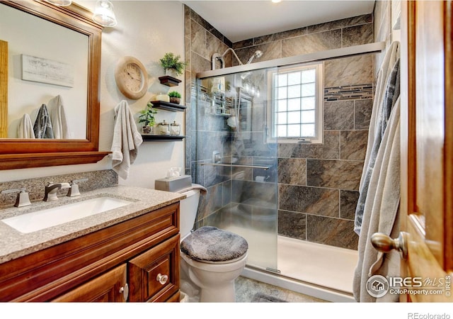 bathroom featuring a shower with shower door, toilet, and vanity