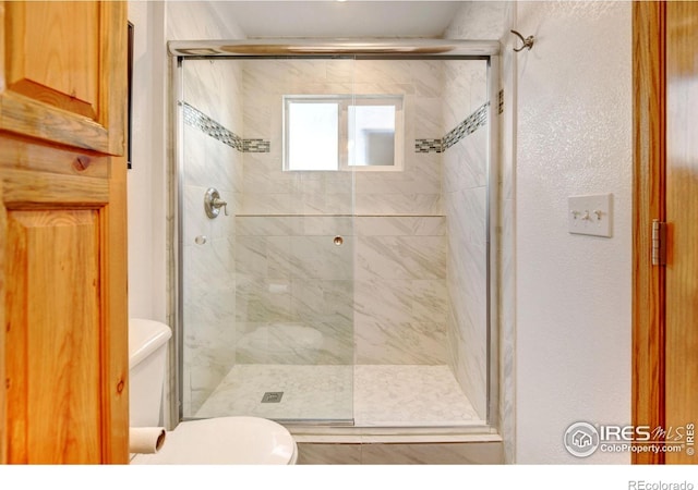 bathroom featuring a shower with door and toilet