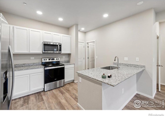 kitchen with light wood-type flooring, a peninsula, a sink, and stainless steel appliances