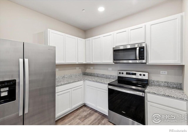 kitchen featuring white cabinets, light stone countertops, stainless steel appliances, and light wood-type flooring