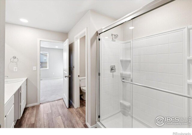 bathroom with wood-type flooring, walk in shower, vanity, and toilet