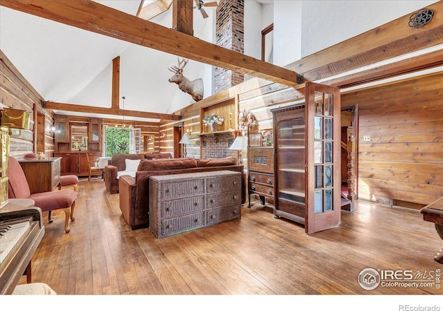 living room featuring wood walls, wood-type flooring, beam ceiling, high vaulted ceiling, and ceiling fan