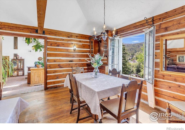 dining space with a chandelier, wooden walls, light wood-type flooring, and lofted ceiling