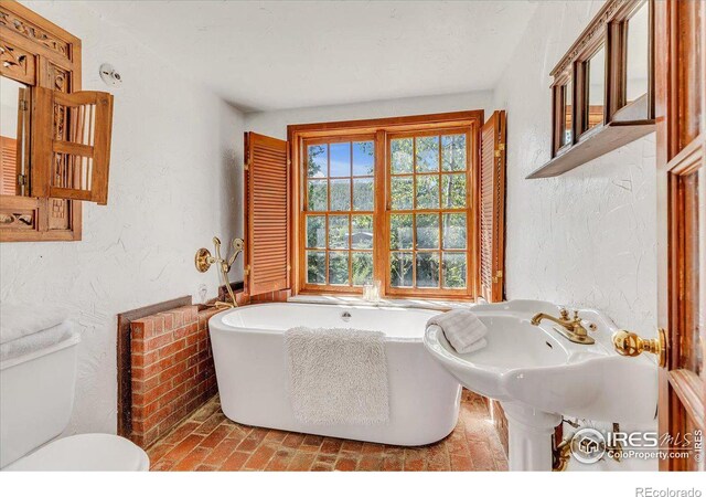 bathroom with a tub to relax in and toilet