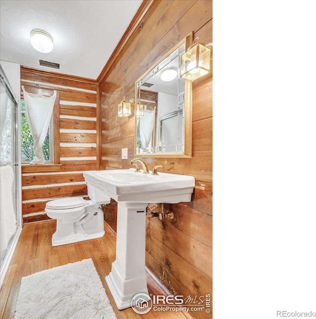 bathroom featuring wood walls, toilet, ornamental molding, and wood finished floors