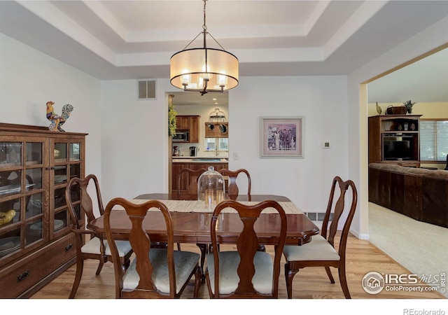 dining area with a notable chandelier, visible vents, a raised ceiling, and light wood-style floors