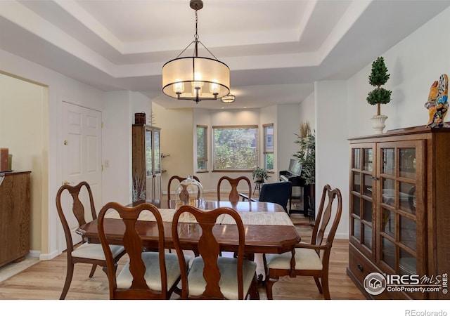 dining area with baseboards, a raised ceiling, an inviting chandelier, and light wood finished floors