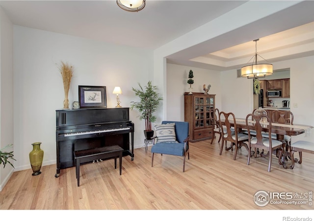 sitting room featuring a tray ceiling, baseboards, and light wood-style floors