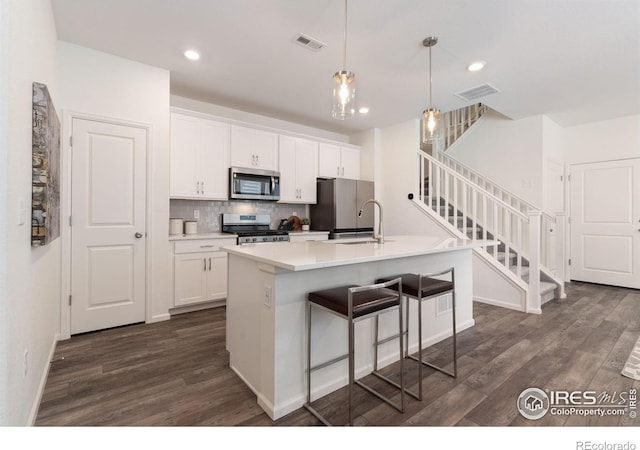 kitchen featuring white cabinetry, a center island with sink, dark wood-type flooring, and appliances with stainless steel finishes