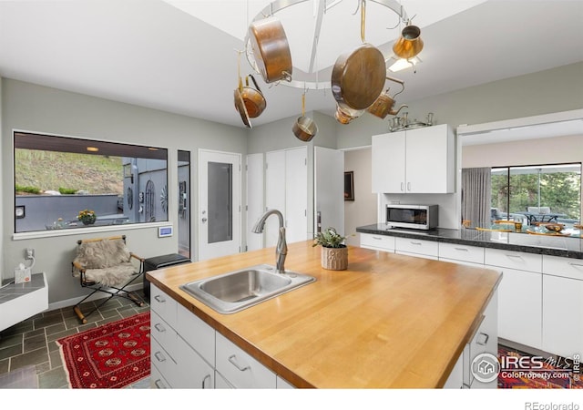 271 Anemone Dr, Boulder, CO 80302 - kitchen with wooden counters, stainless steel microwave, white cabinets, dark stone finish flooring, and a center island with sink
