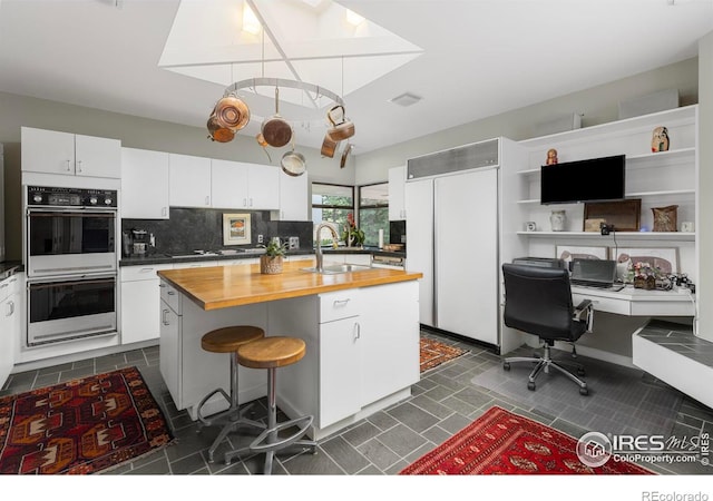 kitchen featuring an island with sink, a breakfast bar, wood counters, and white cabinets