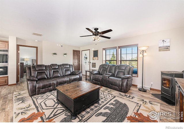 living area featuring visible vents, a ceiling fan, a wood stove, light wood-type flooring, and baseboards