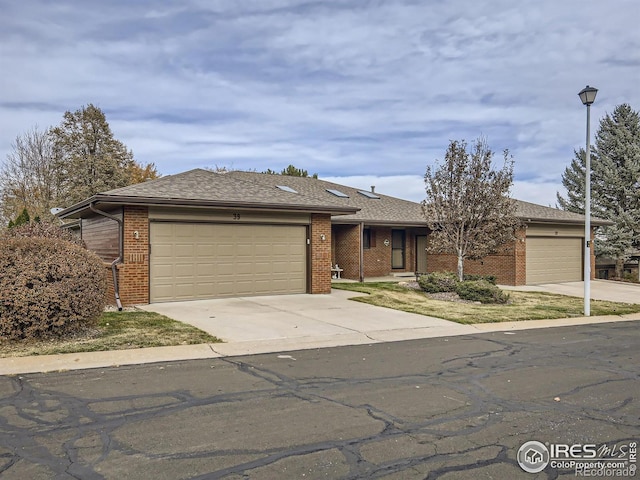 ranch-style house featuring concrete driveway, an attached garage, brick siding, and roof with shingles