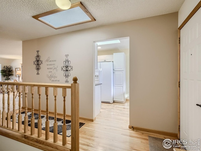 corridor featuring light wood-type flooring, an upstairs landing, a textured ceiling, and baseboards