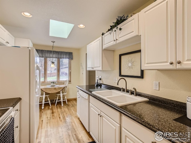 kitchen featuring light wood-style flooring, a skylight, white appliances, white cabinetry, and a sink