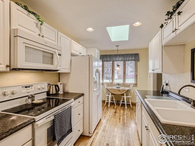 kitchen featuring light wood finished floors, a skylight, white cabinets, white appliances, and a sink