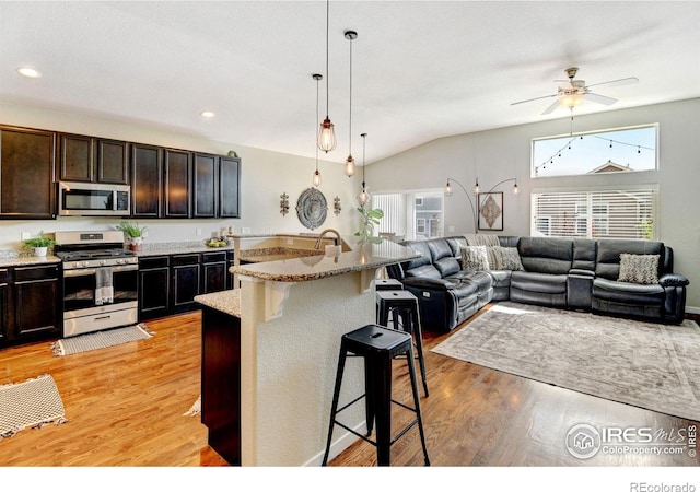 kitchen featuring pendant lighting, stainless steel appliances, a kitchen breakfast bar, light stone counters, and lofted ceiling