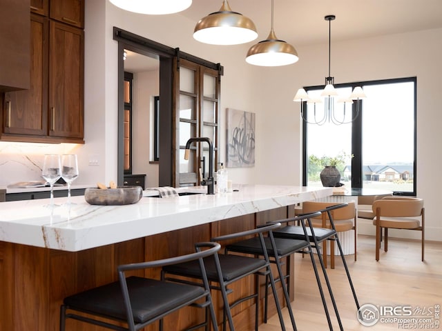 kitchen featuring light stone countertops, a barn door, kitchen peninsula, hanging light fixtures, and light hardwood / wood-style floors