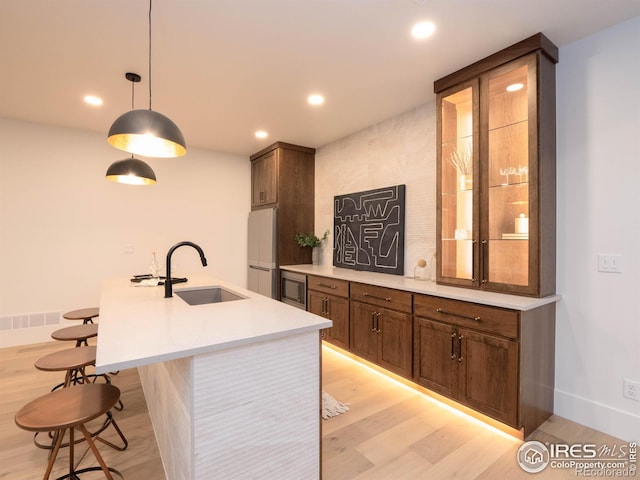 kitchen with an island with sink, a kitchen breakfast bar, light wood-type flooring, sink, and white refrigerator