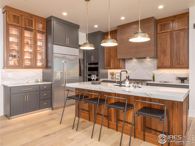 kitchen with an island with sink, light stone countertops, light hardwood / wood-style flooring, pendant lighting, and stainless steel appliances