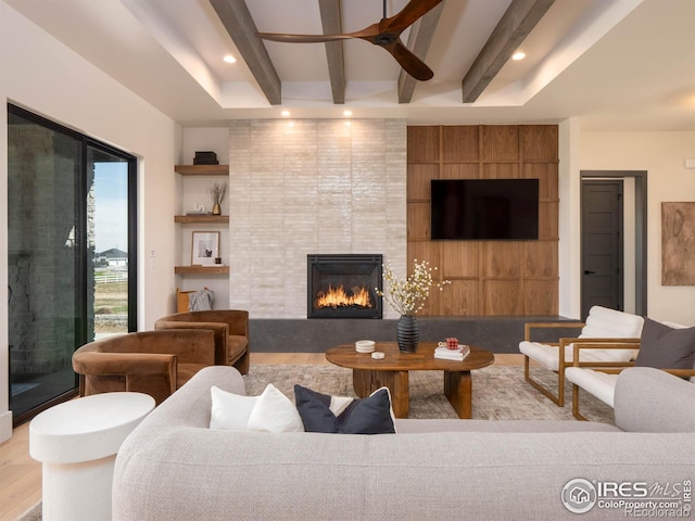 living room with beamed ceiling, a tile fireplace, light wood-type flooring, and ceiling fan