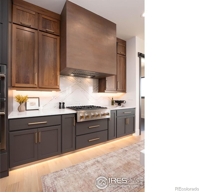 kitchen with decorative backsplash, custom exhaust hood, light hardwood / wood-style flooring, and stainless steel gas cooktop