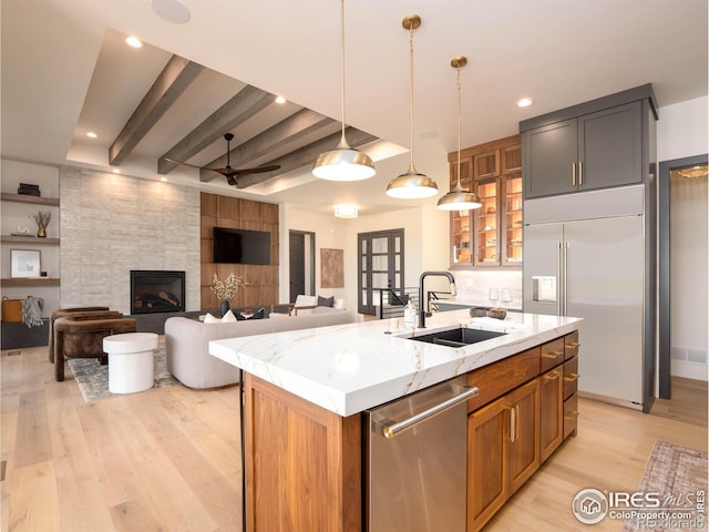 kitchen with hanging light fixtures, a center island with sink, appliances with stainless steel finishes, light stone countertops, and beamed ceiling