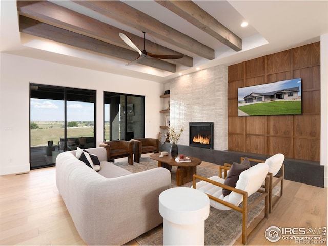 living room with beamed ceiling, a fireplace, light hardwood / wood-style floors, and wood walls